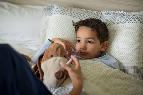 chory młody chłopiec leżący w łóżku i zażywający leki - Zdjęcie, obraz