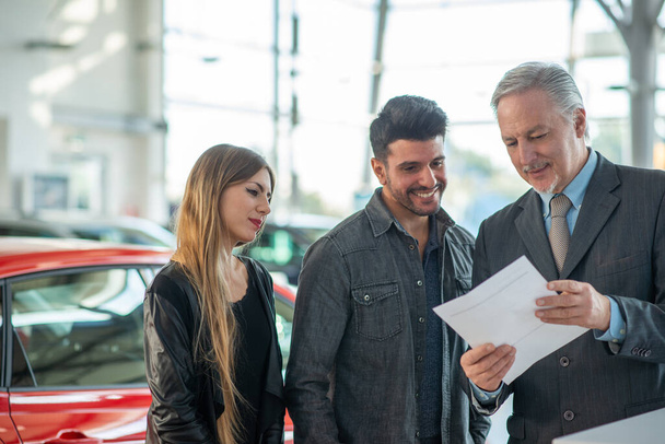 Young family talking to the salesman and choosing their new car in a showroom - 写真・画像