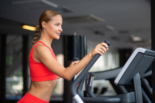 Woman training on the elliptical machine in a gym - Foto, afbeelding