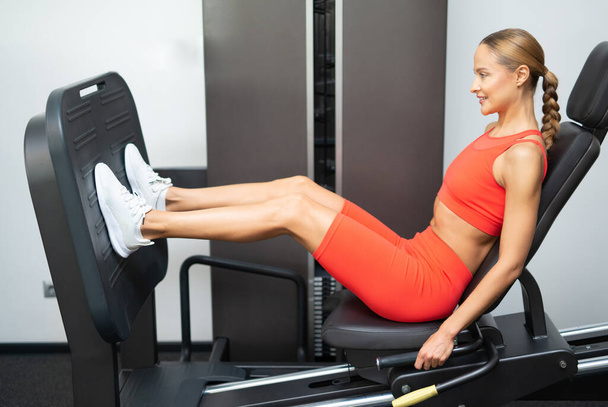 Woman using a leg press machine in a fitness club - Foto, imagen