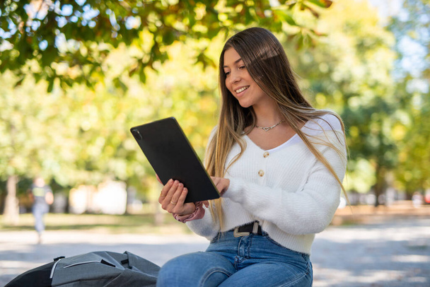 Young woman using a digital tablet sitting on a bench in a park - Φωτογραφία, εικόνα
