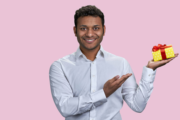 Retrato de indio publicitando una caja de regalo. Aislado sobre fondo rosa. - Foto, imagen