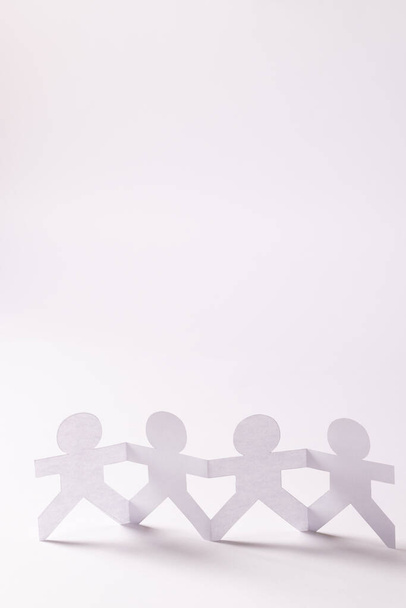 Close up of four paper cut out people figures holding hands with copy space on white background. Humanitarian, people, help and human concept. - Photo, Image