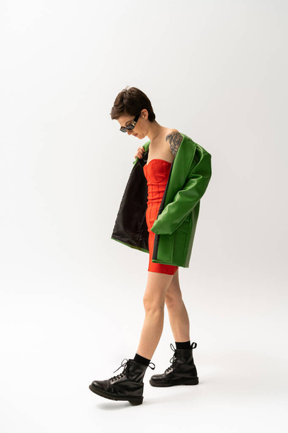 comprimento total da mulher tatuada em jaqueta de couro verde e botas pretas no fundo cinza - Foto, Imagem