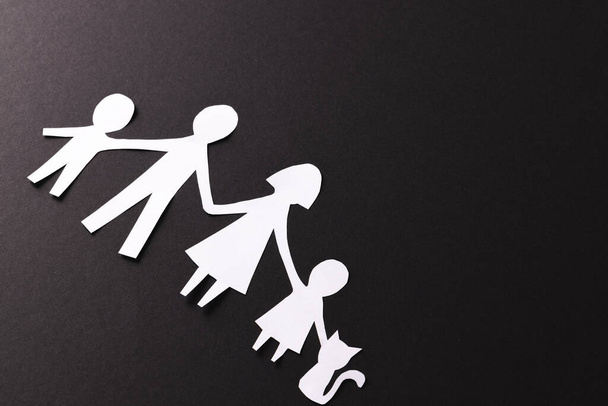 White paper cut out of family with two children and cat and copy space on black background. Humanitarian aid, people, help and human concept. - Фото, зображення