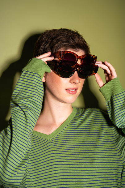 fiatal nő divatos csíkos pulóver visel több napszemüveg zöld háttér - Fotó, kép