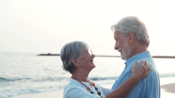 beelden van twee vrolijke en actieve senioren of gepensioneerden die plezier hebben en genieten van de zonsondergang lachend met de zee - oude mensen die samen op vakantie gaan - Video