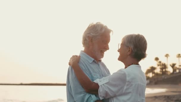 кадры двух счастливых и активных пожилых людей или пенсионеров, веселящихся и наслаждающихся видом на закат, улыбающихся с морем - пожилые люди на открытом воздухе, наслаждающиеся отпуском вместе - Кадры, видео