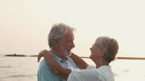 footage of two happy and active seniors or pensioners having fun and enjoying looking at the sunset smiling with the sea - old people outdoors enjoying vacations together - Footage, Video