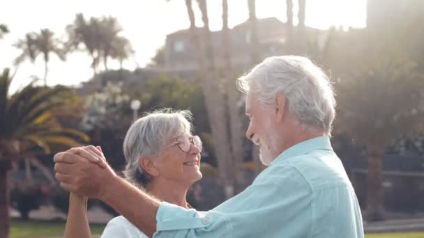 beelden van twee vrolijke en actieve senioren of gepensioneerden die plezier hebben en genieten van de zonsondergang lachend met de zee - oude mensen die samen op vakantie gaan - Video