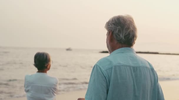Filmaufnahmen von zwei glücklichen und aktiven Senioren oder Rentnern, die Spaß haben und den Sonnenuntergang lächelnd mit dem Meer betrachten - alte Menschen, die ihren Urlaub zusammen genießen - Filmmaterial, Video