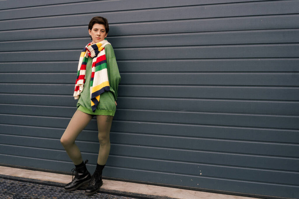 full length of woman in striped scarf and black leather boots posing near grey wall on street - Photo, image