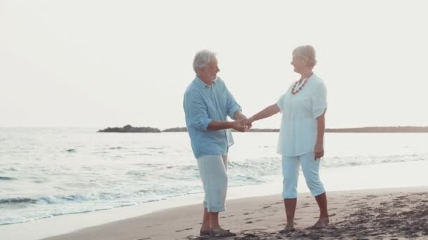 πλάνα από δύο χαρούμενους και δραστήριους ηλικιωμένους ή συνταξιούχους που διασκεδάζουν και απολαμβάνουν να βλέπουν το ηλιοβασίλεμα χαμογελώντας με τη θάλασσα - ηλικιωμένοι σε εξωτερικούς χώρους απολαμβάνοντας τις διακοπές τους μαζί - Πλάνα, βίντεο