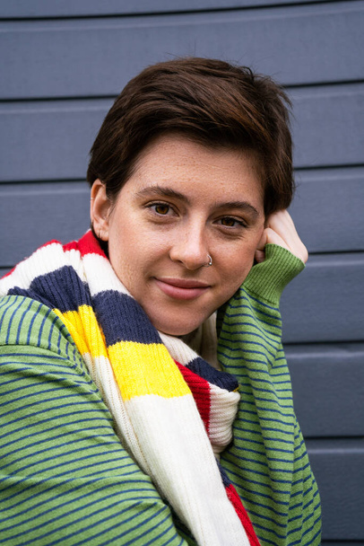 portrait of carefree freckled woman in striped multicolored scarf looking at camera near grey wall on street - Foto, imagen