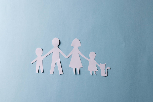 White paper cut out of family with two children and cat and copy space on blue background. Humanitarian aid, people, help and human concept. - Fotó, kép