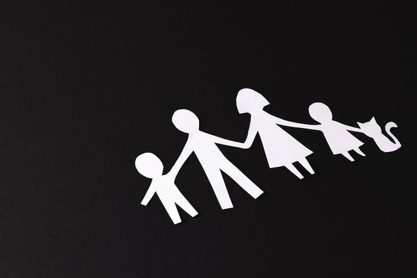 White paper cut out of family with two children and cat and copy space on black background. Humanitarian aid, people, help and human concept. - Foto, Imagem