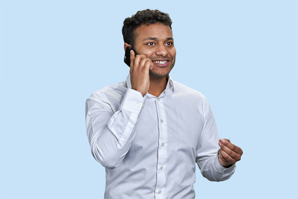 Handsome young indian man talking on the mobile phone. Good talk with friend. Isolated on pale blue background. - Photo, image