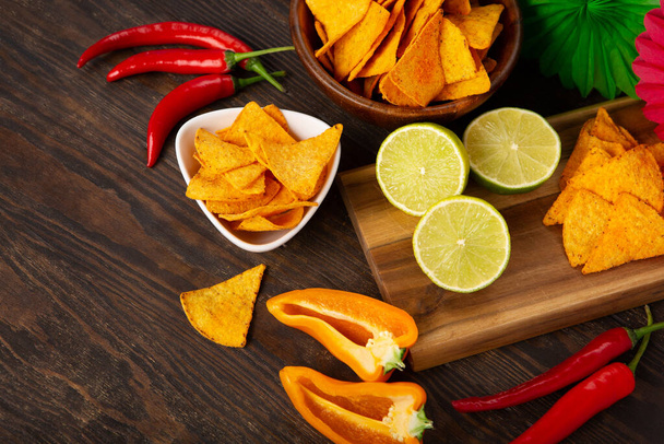 Cinco de Mayo (5. května) koncepce oslav. Mexická pozadí fiesta s tradičními mexickými nachos chipsy, červené chilli papričky, zelené vápno na tmavém dřevěném pozadí. Horní pohled, kopírovací prostor. - Fotografie, Obrázek