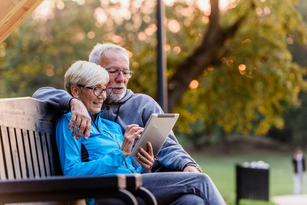couple aîné avec tablette sur banc dans le parc - Photo, image