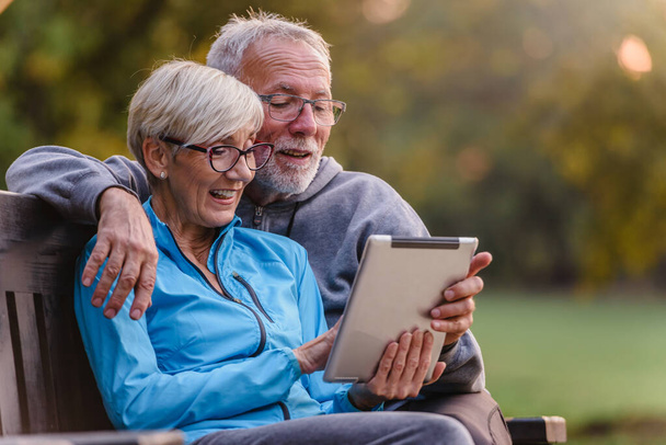 ηλικιωμένο ζευγάρι με tablet στον πάγκο στο πάρκο - Φωτογραφία, εικόνα