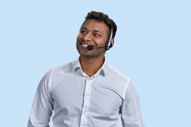 Portrait of a young smiling indian man with headset. Businessman or customer support worker. Isolated on blue. - Fotografie, Obrázek
