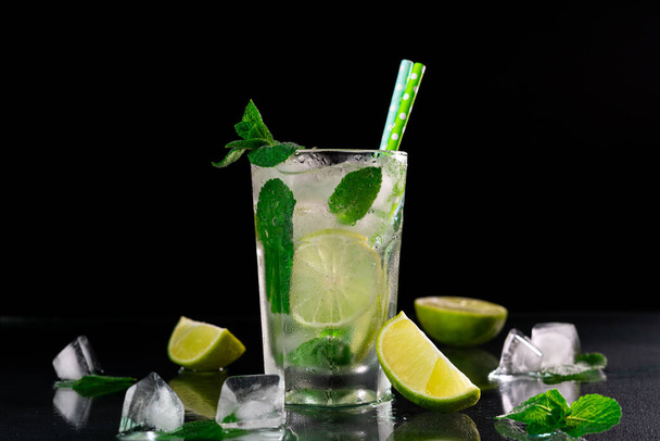 Erfrischender Mojito-Cocktail mit Limette, Eiswürfeln und grünen Minzblättern auf schwarzem Hintergrund - Foto, Bild