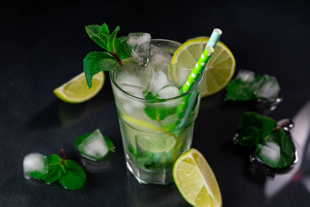 Refreshing Mojito Cocktail with lime, ice cubes and green mint leaves on a black background - Φωτογραφία, εικόνα