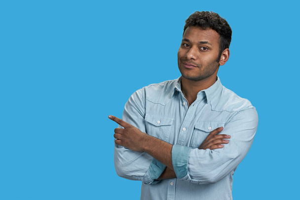 Portrait of south asian arabic guy with folded arms pointing at copy space. Isolated on vivid blue background. - Foto, Imagem