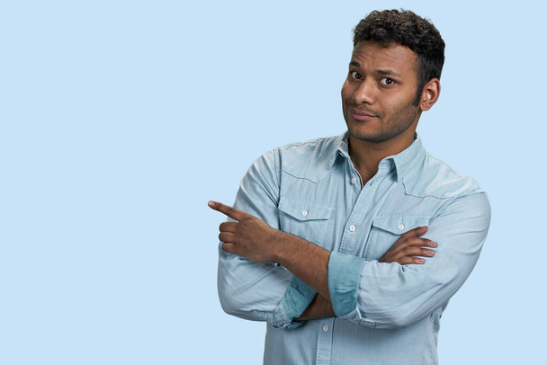 South asian brown guy with folded arms pointing at copy space. Isolated on pastel blue background. - Fotó, kép