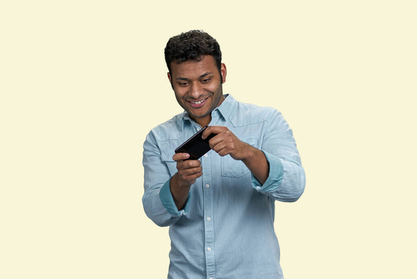 モバイルゲームでゲームをプレイする幸せな若いインド人男性ゲーマーを興奮させました。白地に隔離された. - 写真・画像