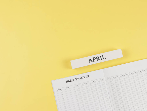 Вид сверху или плоский макет книги Habit tracker, деревянный календарь апрель на желтом фоне с пространством для копирования. - Фото, изображение