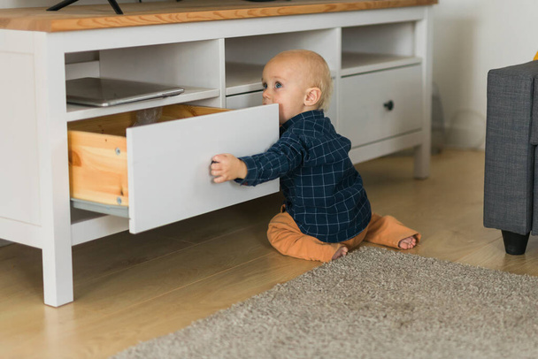 Toddler baby boy open cabinet drawer with his hand. Child explore what is in cabinet. Baby curiosity and child development stages concept - Photo, image
