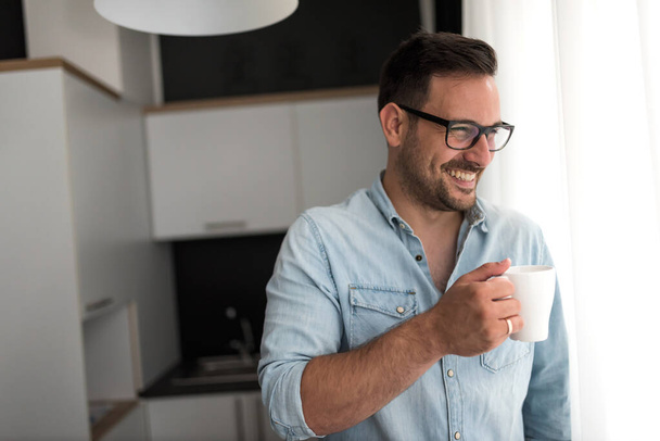 schöner junger Mann mit einer Tasse Kaffee zu Hause - Foto, Bild