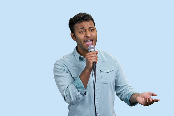 Portrait of a young indian singer with microphone. Southeast asian male on pale blue background. - Zdjęcie, obraz