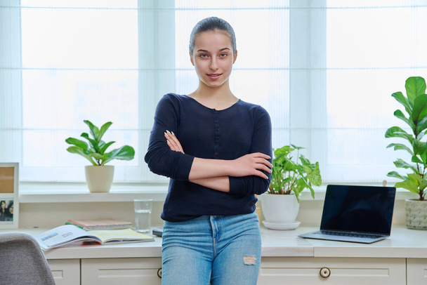 Portrait of teenage girl looking at camera in home interior. Smiling girl 15, 16 years old in casual clothes with crossed arms. Adolescence, lifestyle, leisure, education, learning concept - Zdjęcie, obraz