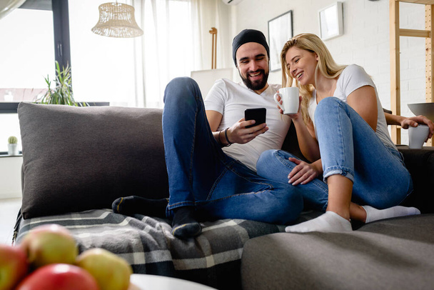 Giovane coppia hipster seduta sul divano a casa a parlare e bere caffè - Foto, immagini