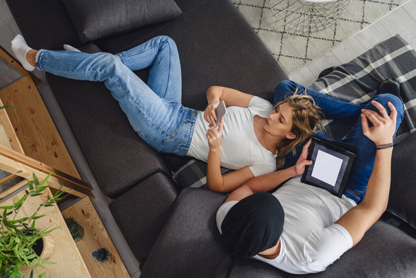 couple relaxing in living room, using gadgets - 写真・画像