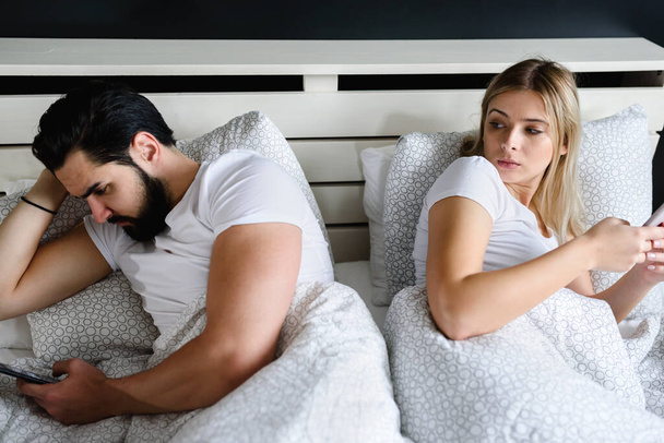junges Paar liegt auf Bett und benutzt Mobiltelefone - Foto, Bild