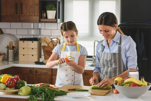 La linda niña ayudando a la madre en la cocina preparando una sabrosa comida vegetariana - Foto, imagen
