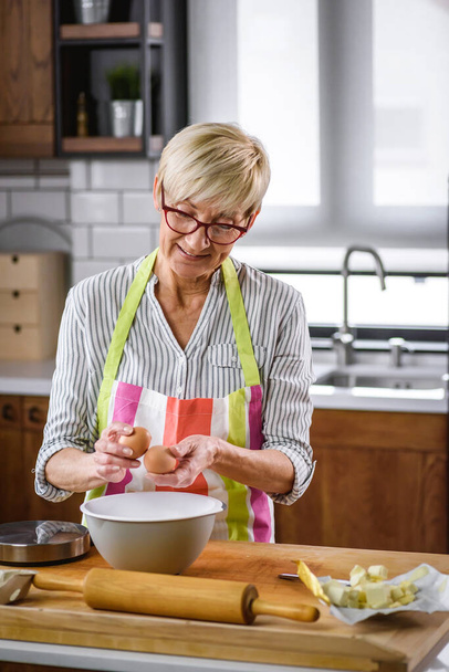 Senior aged woman baking in home kitchen. - Фото, изображение