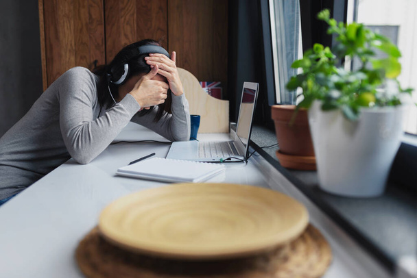 Молодая женщина сидит перед портативным компьютером дома чувствуя себя подавленной - Фото, изображение