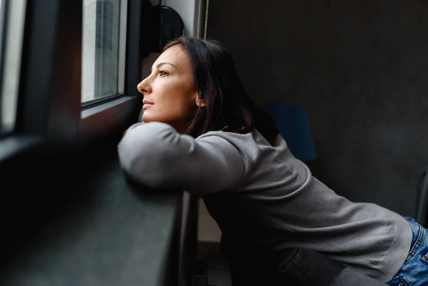 Mujer sentada sola en casa mirando por la ventana - Foto, Imagen