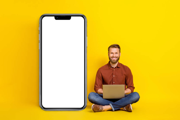 Full size photo of handsome guy sit floor use netbook empty space telephone display isolated on yellow color background. - Φωτογραφία, εικόνα