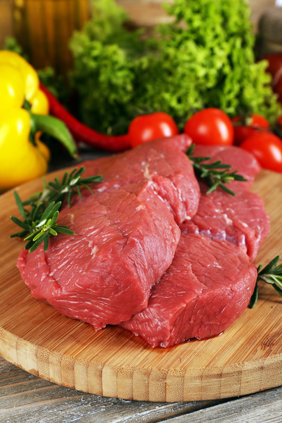 Raw beef steak on cutting board with vegetables and greens on wooden background - Fotó, kép