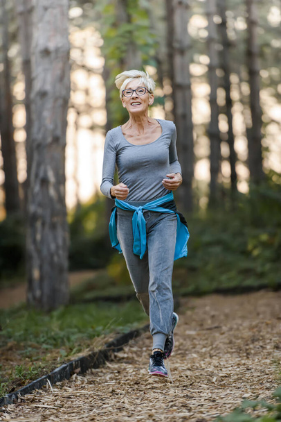 公園でジョギングしている笑顔の先輩女性。高齢者スポーツ活動. - 写真・画像