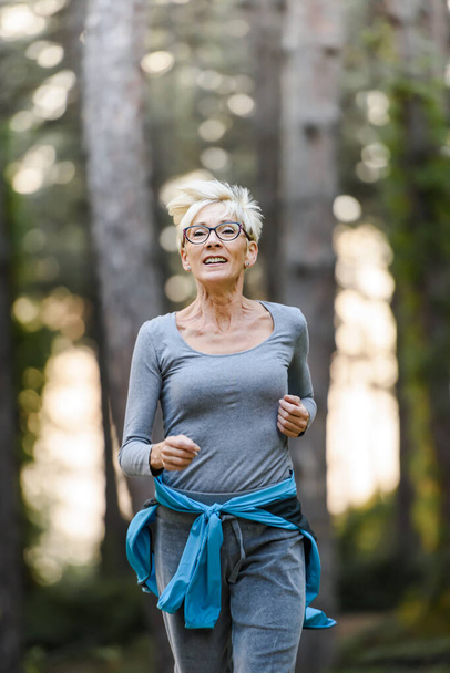 Lachende oudere vrouw joggen in het park. Sportactiviteiten voor ouderen. - Foto, afbeelding