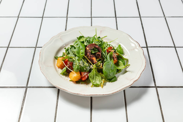 Salada quente com poleiro empanado, polvo, tomate, queijo parmesão e alface. A comida está em uma placa de cerâmica leve. - Foto, Imagem