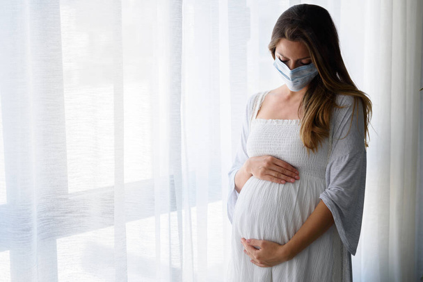 bela mulher grávida usando máscara, de pé no hospital  - Foto, Imagem