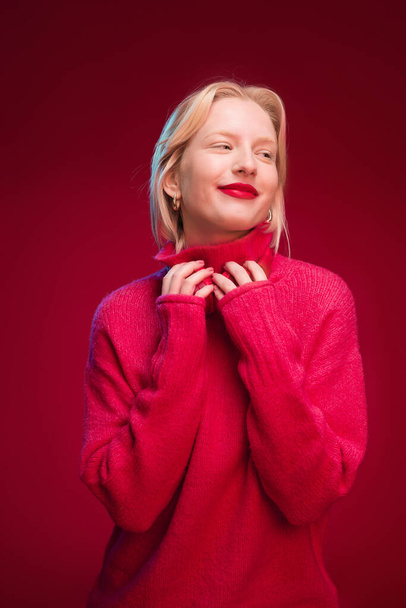 A happy woman standing isolated on red background and posing with headphones. - Valokuva, kuva