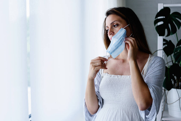 mooie zwangere vrouw met masker, staande in het ziekenhuis  - Foto, afbeelding